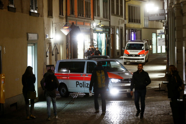  People walk past as Swiss police vehicles stand by to prevent expected illegal gatherings amid restrictions due to the coronavirus (COVID-19) pandemic, in the old town of Zurich, Switzerland, April 9, 2021. (credit: Arnd Wiegmann/Reuters)