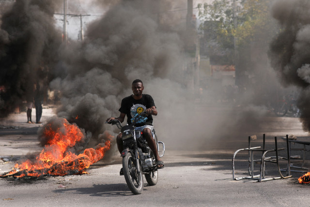  A man drives past a burning barricade during a protest against Prime Minister Ariel Henry's government and insecurity, in Port-au-Prince, Haiti March 1, 2024. (credit: REUTERS)