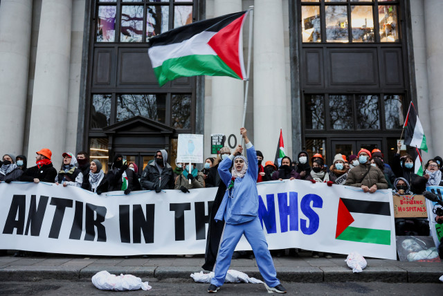  A woman waves a Palestinian flag as picketers from 'Health Workers for a Free Palestine' demonstrate against software company, Palantir Technologies UK, by blocking access to their offices, in London, Britain December 21, 2023. (credit: REUTERS/Isabel Infantes)