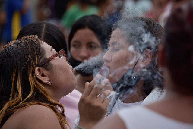  A woman blows cigarette smoke at another woman in the belief that this will help alleviate the effects of tear gas fired by police officers, during a protest to demand fair treatment of their loved ones, outside the Litoral prison in Guayaquil, Ecuador, January 22, 2024. (credit: REUTERS/VICENTE GAIBOR DEL PINO)