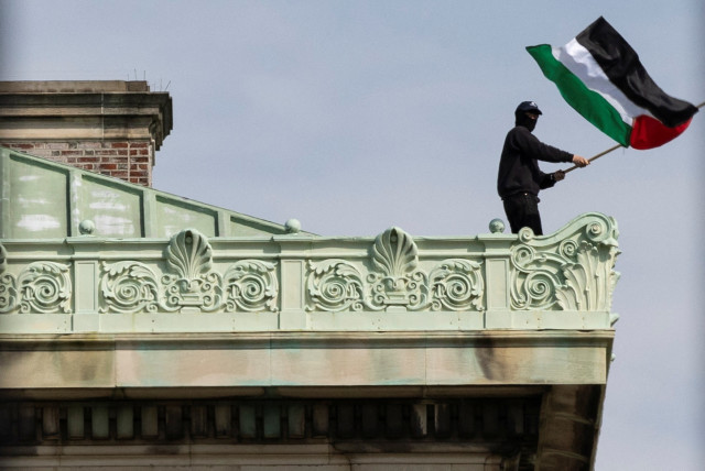  A student protester waves a Palestinian flag from the roof of Hamilton Hall, where students at Columbia University have barricaded themselves as they continue to protest in support of Palestinians, April 30, 2024. (credit: REUTERS/CAITLIN OCHS)