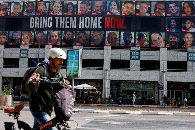  Un hombre empuja una bicicleta cerca de una valla publicitaria con imágenes de los rehenes secuestrados en el mortífero ataque del 7 de octubre contra Israel por el grupo islamista palestino Hamás desde Gaza, en Tel Aviv, Israel 18 de marzo de 2024. (credit: CARLOS GARCIA RAWLINS/REUTERS)