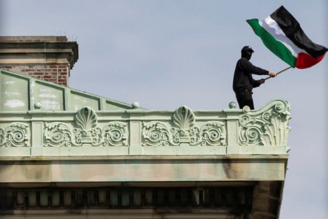  Un estudiante protesta ondeando una bandera palestina desde el tejado del Hamilton Hall, donde los estudiantes de la Universidad de Columbia se han atrincherado mientras continúan protestando en apoyo a los palestinos, 30 de abril de 2024. (credit: REUTERS/CAITLIN OCHS)