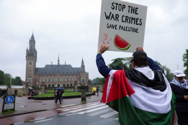 A protester draped in a Palestinian flag holds up a sign at a protest in support of Palestinians in Gaza outside the International Court of Justice (ICJ), on the day of a ruling on South Africa's request to order a halt to Israel's Rafah offensive in Gaza as part of a larger case brought before the  (credit: JOHANNA GERON/REUTERS)