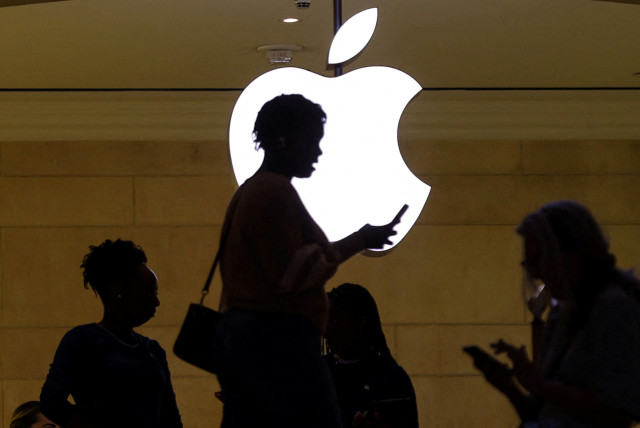  A women uses an iPhone mobile device as she passes a lighted Apple logo at the Apple store at Grand Central Terminal in New York City, US, April 14, 2023. Uploaded on 31/5/2024 (credit: MIKE SEGAR / REUTERS)