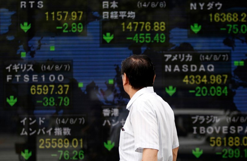 A pedestrian looks at an electronic board showing the stock market indices of various countries outside a brokerage in Tokyo. (photo credit: REUTERS)