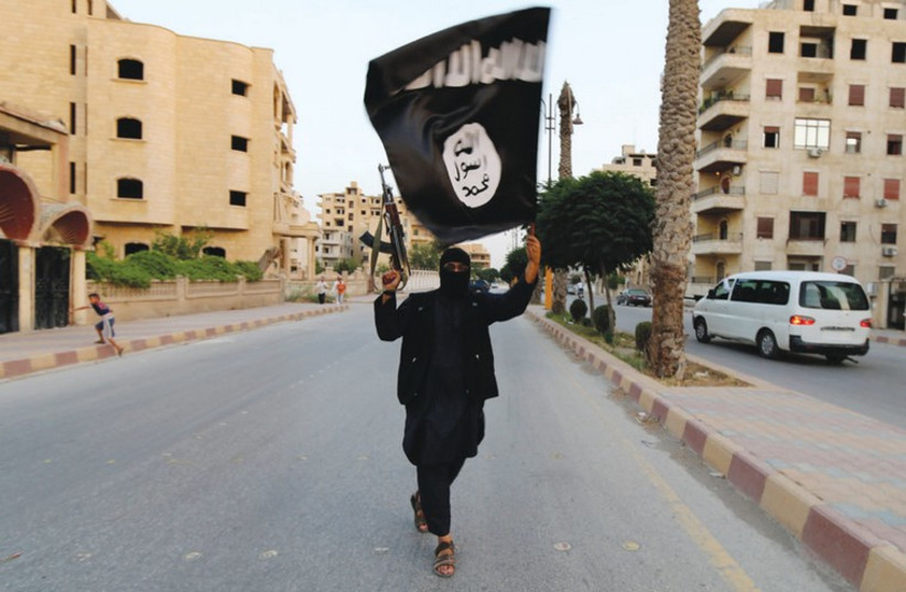 An Islamic State fighter carries the group’s flag in Raqqa, north-central Syria. (photo credit: REUTERS)