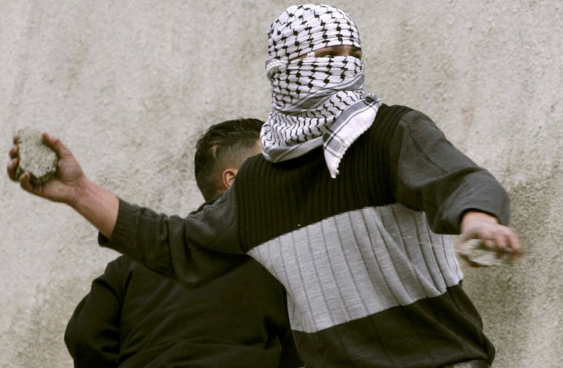 A masked Palestinian teenager throws a stone at Israeli soldiers (photo credit: REUTERS)