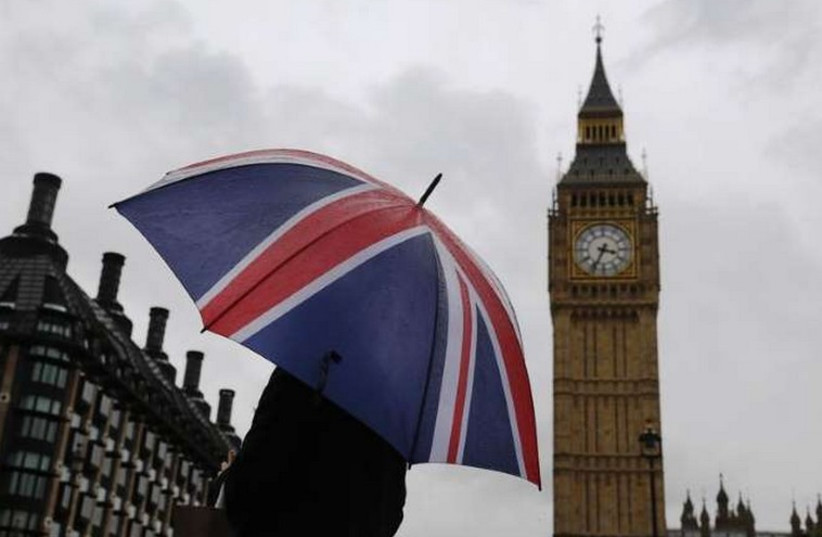 A woman holds a Union flag umbrella in front of the Big Ben clock tower (R) and the Houses of Parliament in London (photo credit: REUTERS)