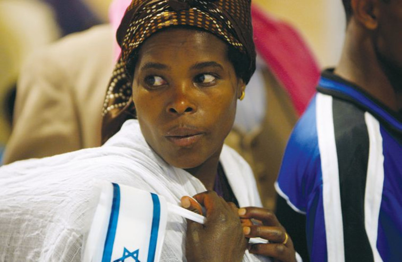 An immigrant from Ethiopia holds an Israeli flag as she carries her child upon her arrival at Ben-Gurion International Airport in January 2011. (photo credit: REUTERS)