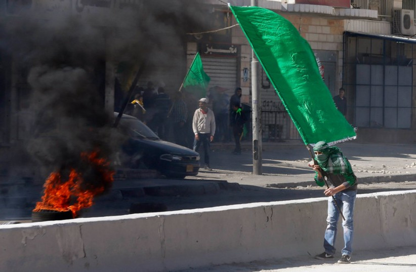 A Palestinian protester holds a Hamas flag during clashes with Israeli troops in the West Bank  (photo credit: REUTERS)