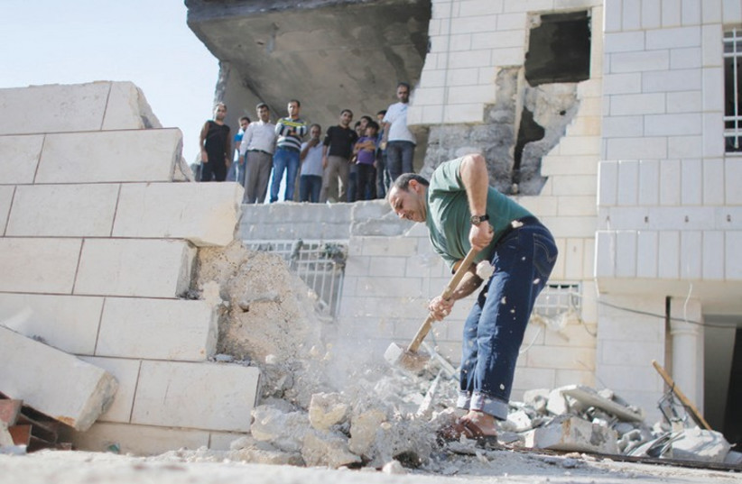 A PALESTINIAN removes a wall to allow a bulldozer access to clear the rubble at the home of Amer Abu Aysha in Hebron in August. The IDF earlier destroyed the home of Abu Aysha, one of the two main suspects in the June kidnapping and murder of three teenagers. (photo credit: AMMAR AWAD / REUTERS)