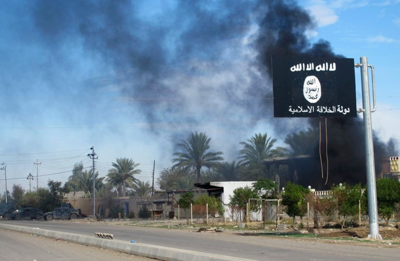 Smoke raises behind an Islamic State flag in Iraq  (photo credit: REUTERS)