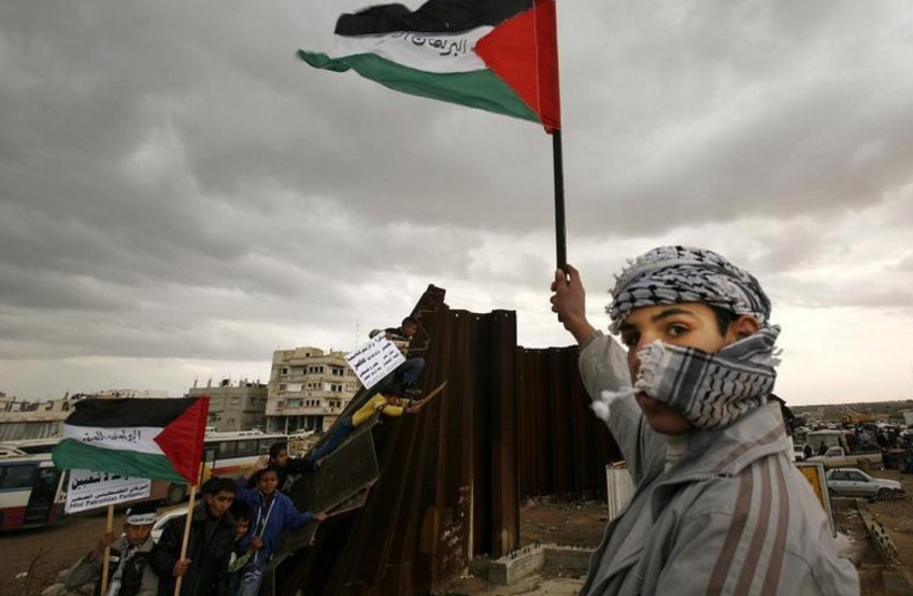 A Palestinian waves a flag near a destroyed section of the border wall between the Gaza Strip and Egypt (photo credit: REUTERS)