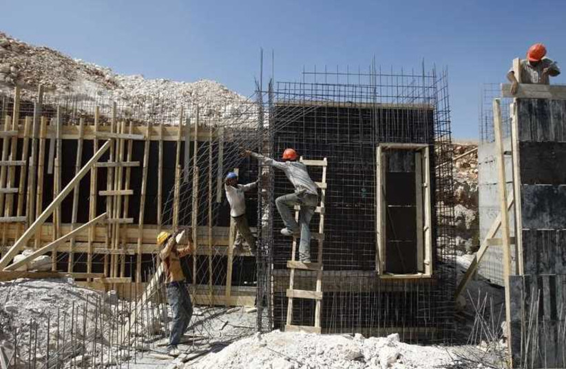 Palestinian laborers work at a construction site in a settlement near Jerusalem  (photo credit: REUTERS)