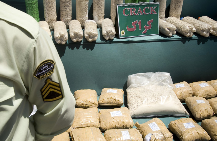 An Iranian anti-narcotics policeman stands guard beside a display of confiscated drugs (photo credit: CAREN FIROUZ / REUTERS)