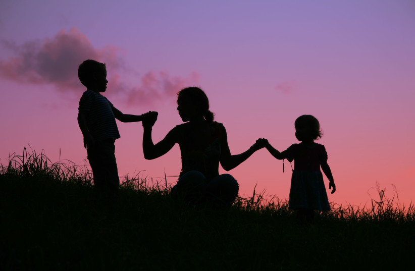 A mother holds two children by the hands during a sunset (photo credit: INGIMAGE)