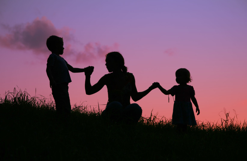 A mother holds two children by the hands during a sunset