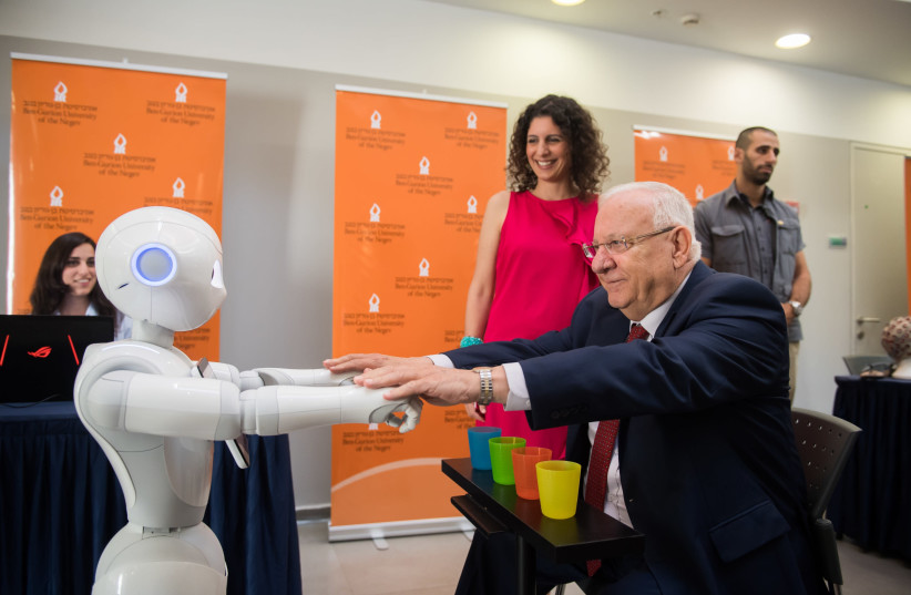 Dr. Shelly Levy-Tzedek (in red dress) demonstrates to President Rivlin how she uses robots for physical therapy during the president’s visit to BGU. Lab Engineer Avital Elishay (at the computer) is running the demonstration. (photo credit: DANI MACHLIS/BGU)