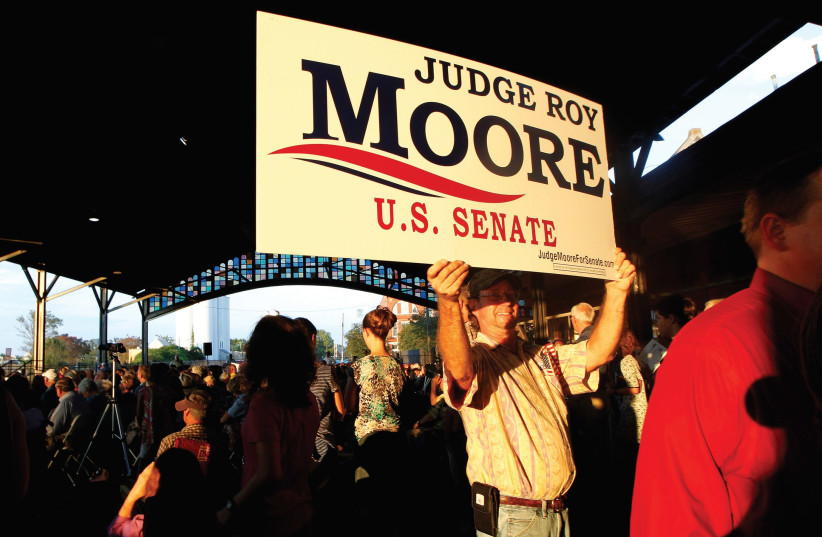 A supporter of US Senate candidate Judge Roy Moore holds a sign as he waits for a campaign rally in Montgomery, Alabama, earlier this year. (photo credit: REUTERS)