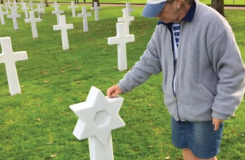 A VISITOR to the American military cemetery in Normandy places a stone on the grave of one of the 300 Jewish soldiers interred there. (photo credit: STEWART WEISS)