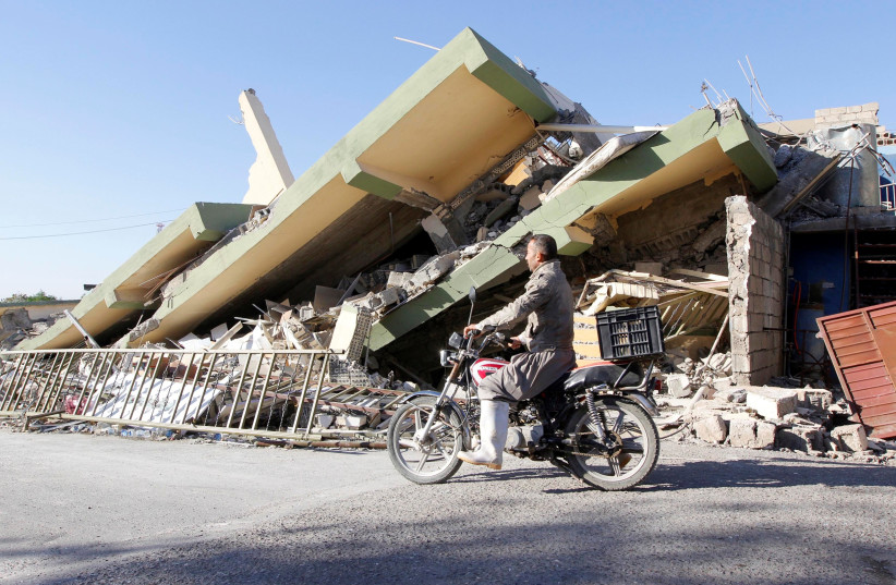 A man rides past the remains of a building in Darbandikhanm, Kurdistan, after a 7.2 magnitude earthquake there, November 2017 (photo credit: AKO RASHEED / REUTERS)
