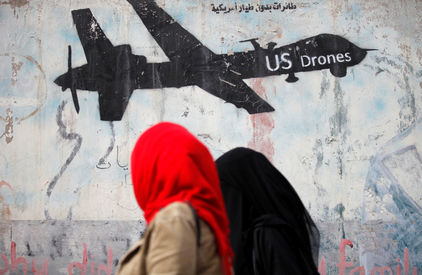 Women walk past a graffiti, denouncing strikes by US drones in Yemen, painted on a wall in Sanaa, Yemen. (photo credit: REUTERS)