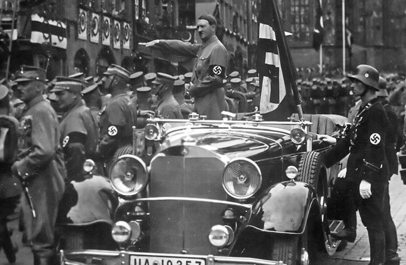 Adolf Hitler salutes, standing in a Mercedes-Benz vehicle  as SA troops parade past him in Nuremberg, Germany, 1935 (photo credit: WIKIMEDIA COMMONS / CHARLES RUSSELL COLLECTION NARA)