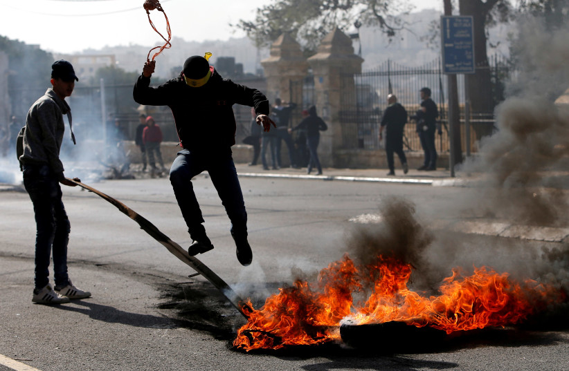 A Palestinian demonstrator jumps over a burning tire in a protest in Bethlehem, January 2018 (photo credit: MUSSA QAWASMA / REUTERS)