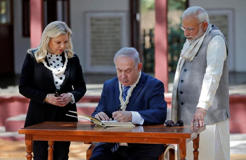 Israeli Prime Minister Benjamin Netanyahu writes a message in the visitor's book as his wife Sara and his Indian counterpart Narendra Modi look on during their visit to Gandhi Ashram in Ahmedabad, India, January 17, 2018.  (photo credit: REUTERS/AMIT DAVE)