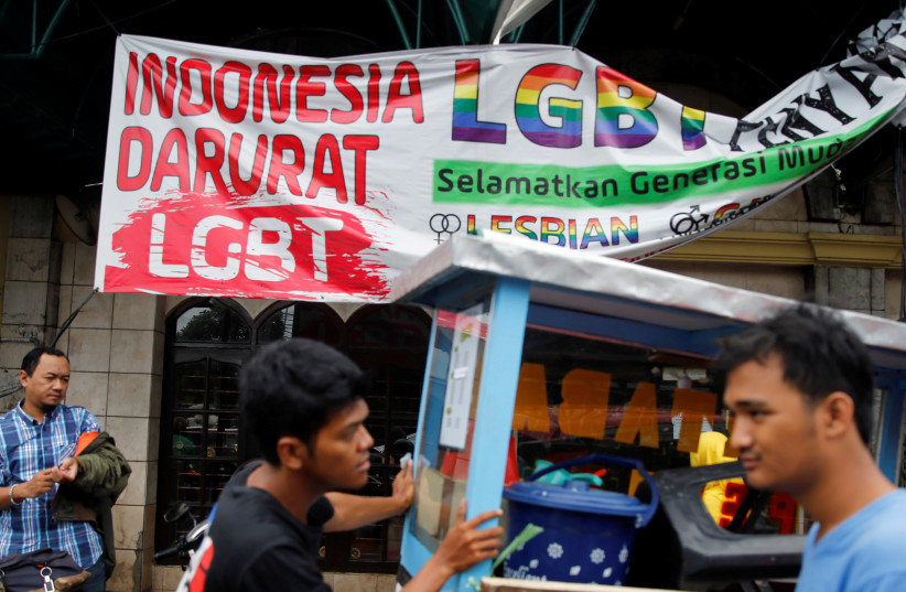 A street vendor walks past a banner reading 'Indonesia LGBT Emergency' in front a mosque in Jakarta, Indonesia (photo credit: BEAWIHARTA BEAWIHARTA/ REUTERS)