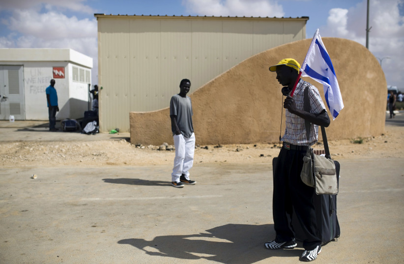 An African migrant holds an Israeli flag after being released from Holot detention centre in Israel's southern Negev desert August 25, 2015. (photo credit: REUTERS/AMIR COHEN)