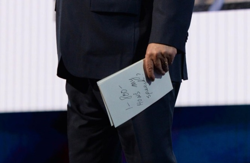 Prime Minister Benjamin Netanyahu holds a booklet showing "1-800 How's My Speech?" at AIPAC Conference (photo credit: CHAIM TZACH/GPO)