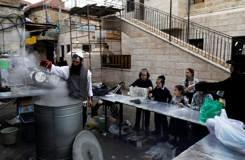 An ultra-Orthodox Jewish man dips cooking utensils in boiling water to remove remains of leaven in preparation for the upcoming Jewish holiday of Passover, in Jerusalem's Mea Shearim neighborhood, March 27, 2018. (photo credit: RONEN ZVULUN/REUTERS)