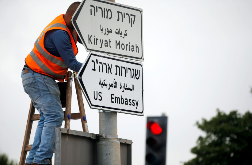 A worker hangs a road sign directing to the US embassy, in the area of the US consulate in Jerusalem, May 7, 2018.  (photo credit: REUTERS/Ronen Zvulun)