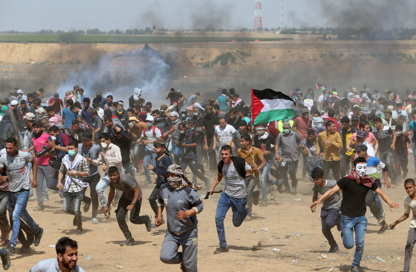 Palestinian demonstrators run for cover from tear gas fired by Israeli forces during a protest at the Israel-Gaza border in the southern Gaza Strip, May 11, 2018 (photo credit: REUTERS/IBRAHEEM ABU MUSTAFA)