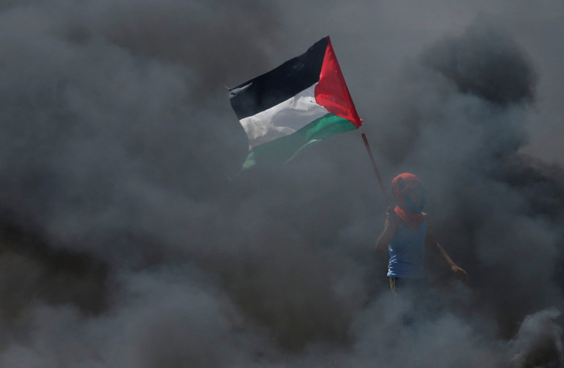  boy holds a Palestinian flag as he stands amidst smoke during a protest at the Israel-Gaza border east of Gaza City May 14, 2018 (photo credit: REUTERS/MOHAMMED SALEM)