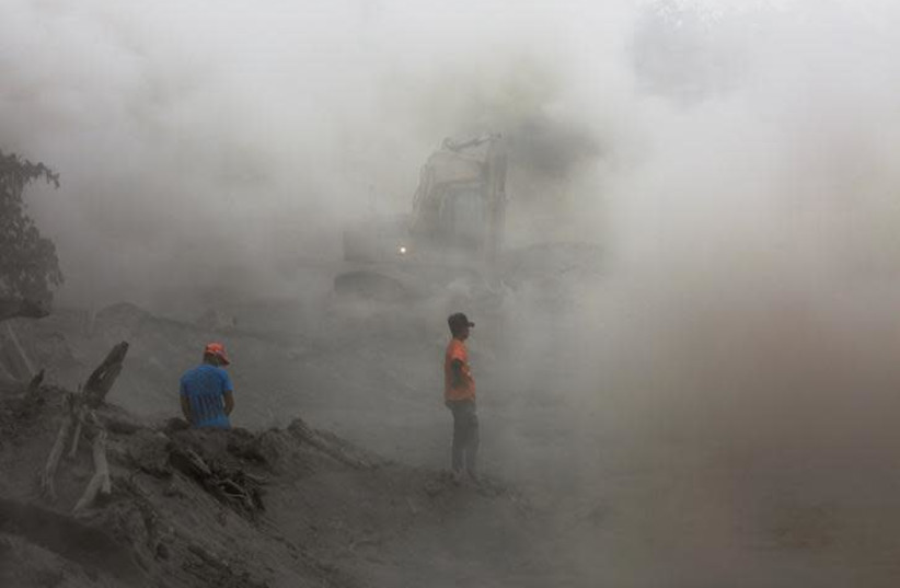 Residents are seen amidst ashes as heavy machinery removes ash from a road at an area affected by the eruption of the Fuego volcano at El Rodeo in Escuintla, Guatemala June 6, 2018. Picture taken June 6, 2018. (photo credit: REUTERS/CARLOS JASSO)