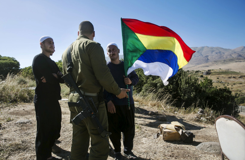 A member of the Druze community holds a Druze flag as he speaks to an Israeli soldier near the border fence between Syria and the Golan Heights, near Majdal Shams June 18, 2015. Gathered at a hilltop in the Golan Heights, a group of Druze sheikhs look through binoculars at the Syrian village of Hade (credit: BAZ RATNER/REUTERS)