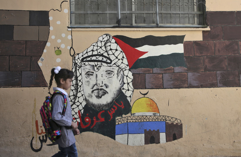 A child walks in front of a mural painting depicting the late Palestinian leader Yasser Arafat on her way to a school run by United Nations Agency for Palestinian Refugees (UNRWA) in Balata refugee camp, east of Nablus on August 29, 2018 (credit: JAAFAR ASHTIYEH / AFP)