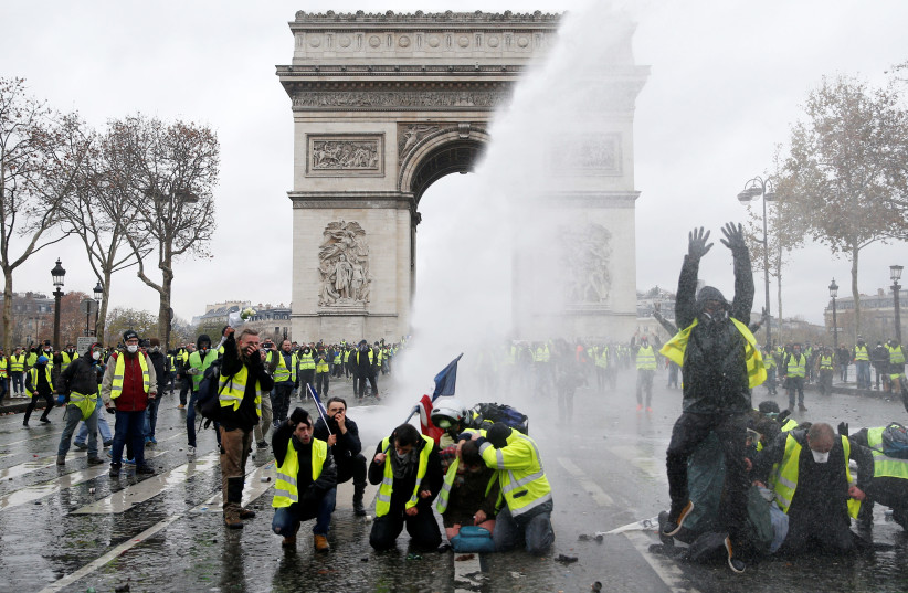 Protesters wearing yellow vests, a symbol of a French drivers' protest against higher diesel taxes, stand up in front of a police water canon at the Place de l'Etoile near the Arc de Triomphe in Paris, France, December 1, 2018 (photo credit: STEPHANE MAHE / REUTERS)