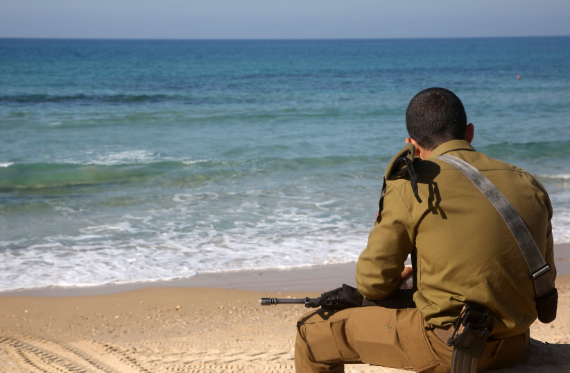 An IDF soldier sits on a beach in Tel Aviv (credit: MARC ISRAEL SELLEM/THE JERUSALEM POST)