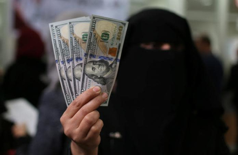A Palestinian Hamas-hired civil servant displays US Dollar banknotes after receiving her salary paid by Qatar, in Khan Yunis in the southern Gaza Strip December 7, 2018. (credit: IBRAHEEM ABU MUSTAFA/REUTERS)