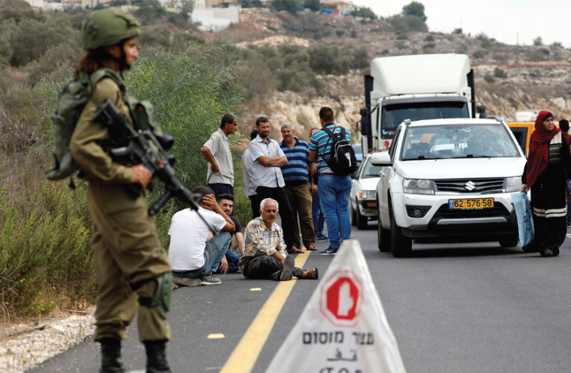 PALESTINIANS WAIT at an IDF checkpoint in the West Bank late last year. (photo credit: MOHAMAD TOROKMAN/REUTERS)