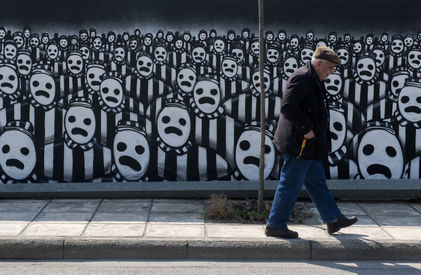 A man walks past a graffiti dedicated to the Holocaust in the northern port city of Thessaloniki (photo credit: ALEXANDROS AVRAMIDIS/REUTERS)