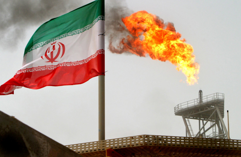 A gas flare on an oil production platform in the Soroush oil fields is seen alongside an Iranian flag in the Persian Gulf, Iran, July 25, 2005 (credit: RAHEB HOMAVANDI/REUTERS)