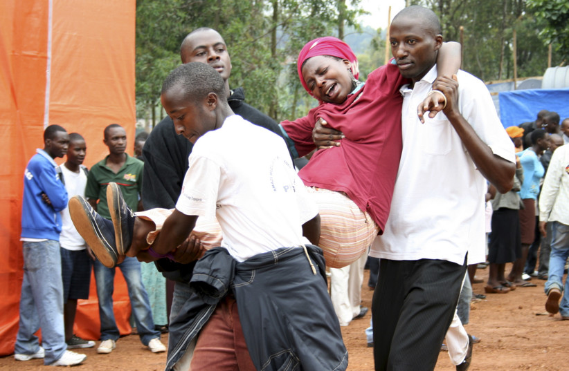 Relatives assist a distressed victim of the genocide at a mass-grave site in Kigali (credit: REUTERS)