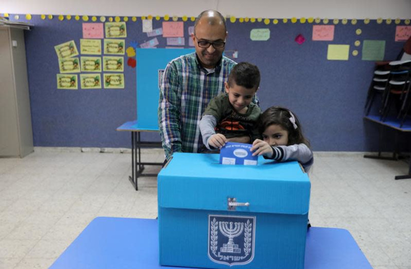 An Israeli-Arab father casts a ballot together with his children, as Israelis vote in a parliamentary election, at a polling station in Umm al-Fahm, Israel April 9, 2019 (photo credit: AMMAR AWAD / REUTERS)