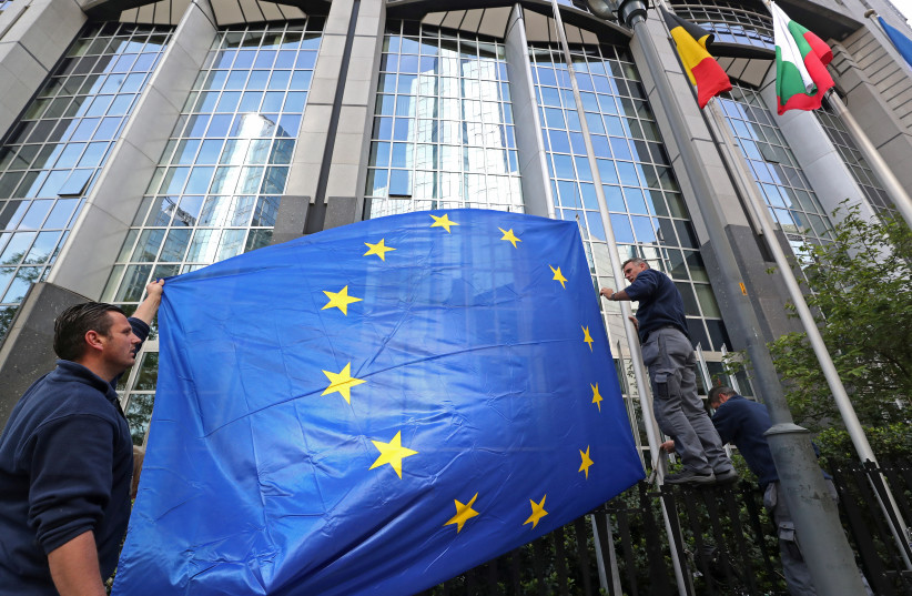 Workers adjust a European flag outside the EU Parliament ahead of the EU elections in Brussels (photo credit: YVES HERMAN / REUTERS)