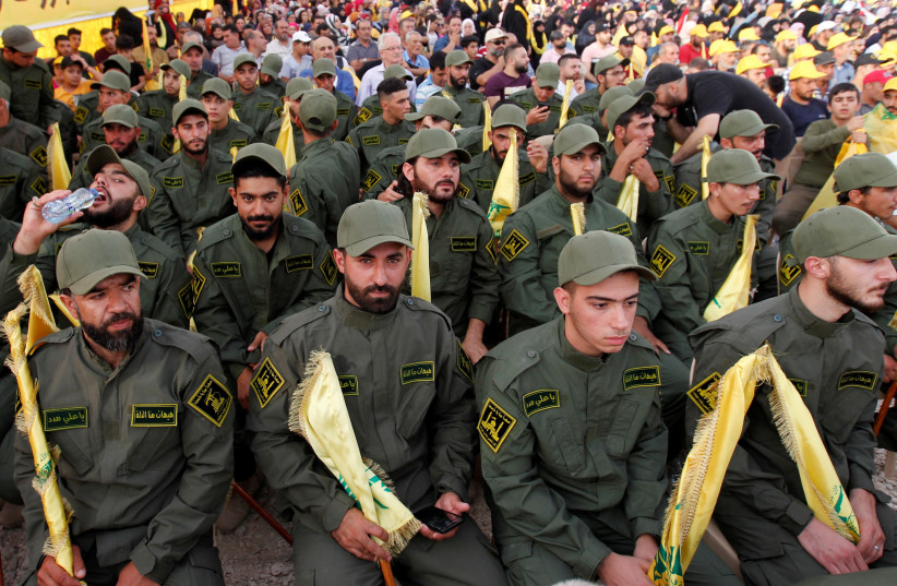 Lebanon's Hezbollah members hold party flags as they listen to their leader Sayyed Hassan Nasrallah addressing his supporters via a screen during a rally marking the anniversary of the defeat of militants near the Lebanese-Syrian border, in al-Ain village, Lebanon August 25, 2019.  (credit: REUTERS)